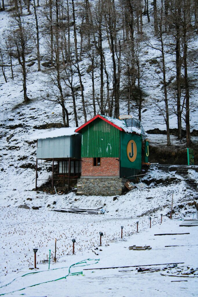 A wooden cabin blanketed in snow at Sissu village in Lahaul Valley, surrounded by Himalayan mountains